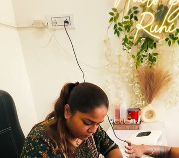 Ruhi working at her studio table under the Ruhi neon sign